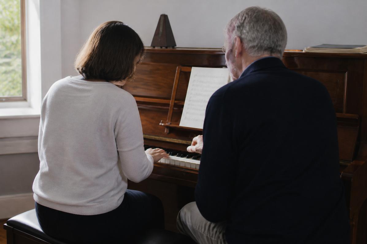 Adult student and teacher seated together at a wooden upright piano